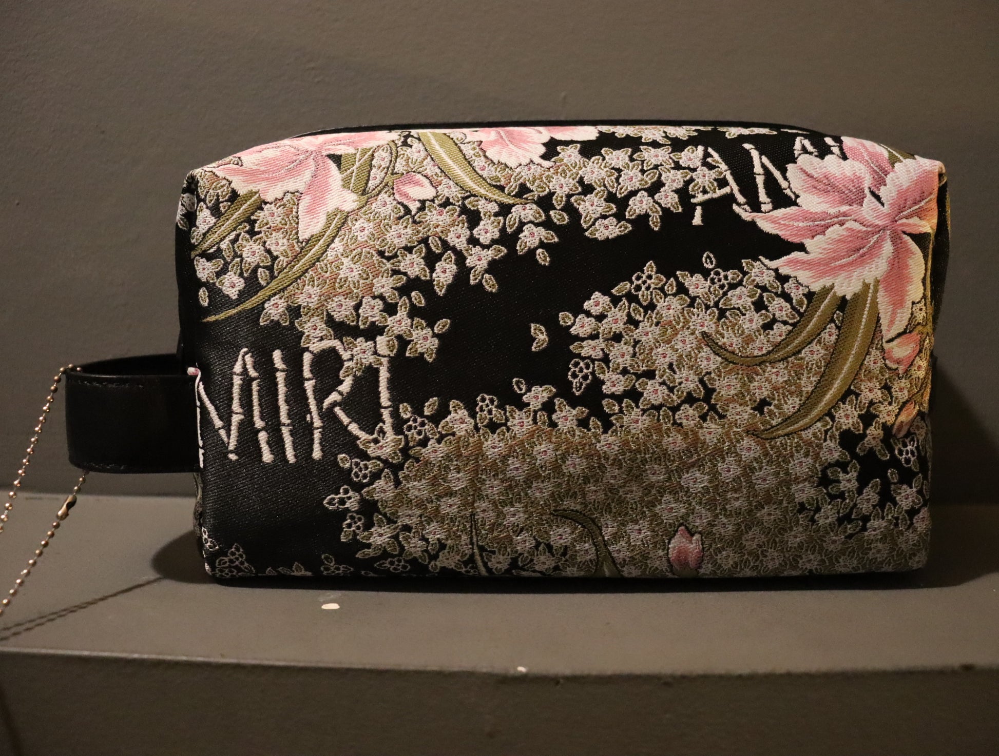 A stylish AMIRI Hibiscus Jacquard Dopp Kit in a multi-colored jacquard fabric, complemented by a twill lining and leather detailing. The AMIRI logo is embroidered on the kit. This kit comes in one size (O/S) and features a vibrant and eye-catching design.
