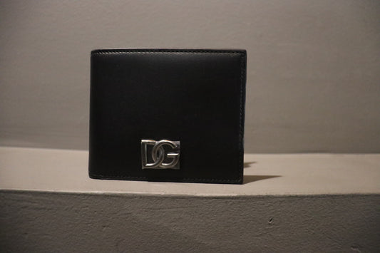 Black Dolce & Gabbana wallet made from calfskin nappa leather, featuring a metal crossover DG logo. The wallet includes a coin pocket, three card slots, two flat side pockets, and one bill compartment. Dimensions are 8.7 x 11 x 2 cm.